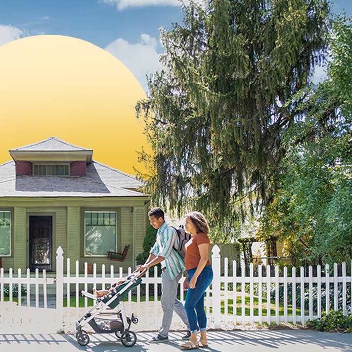 couple walking with baby stroller in front of house with white picket fence